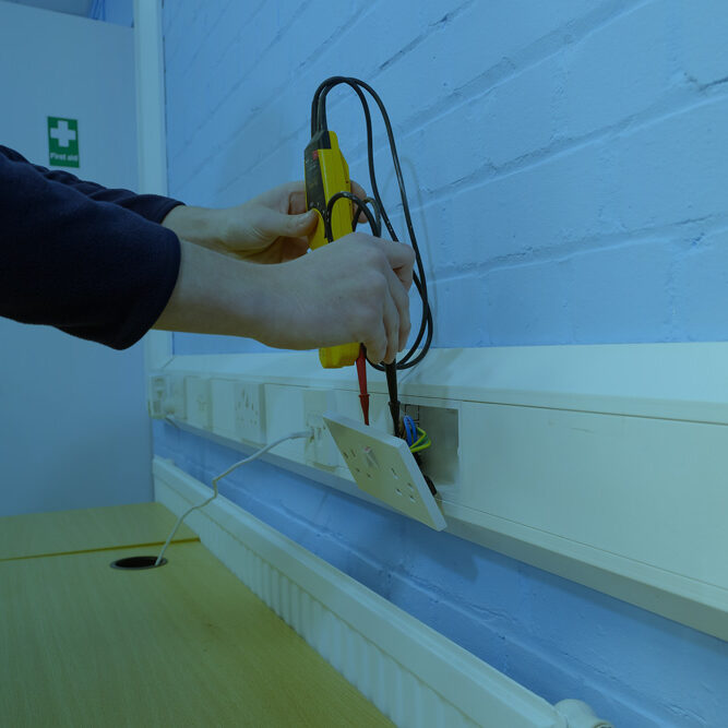 Hand testing a wall socket with a voltage tester