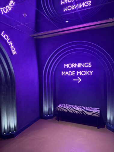 Purple-lit Moxy signage and ceiling detail